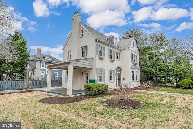 view of front of home featuring a patio area, fence, a front yard, and a chimney