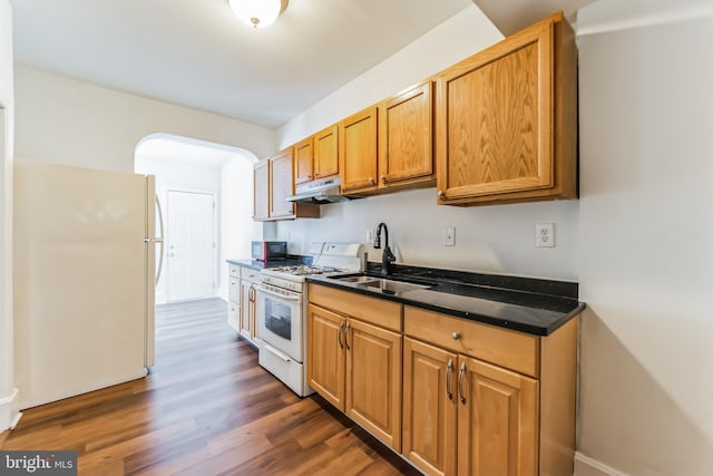 kitchen with white appliances, arched walkways, dark wood-style flooring, under cabinet range hood, and a sink