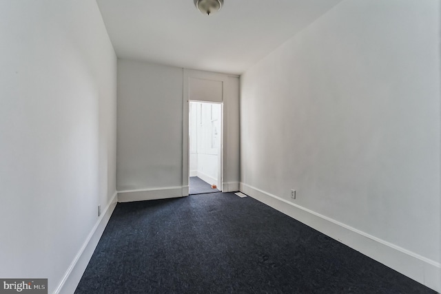 spare room featuring baseboards and dark colored carpet