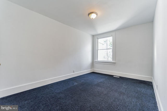 empty room featuring dark colored carpet and baseboards