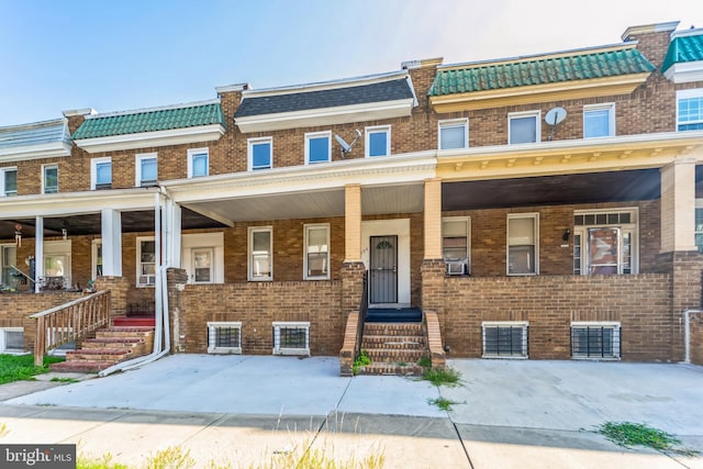 townhome / multi-family property featuring covered porch, mansard roof, cooling unit, and brick siding