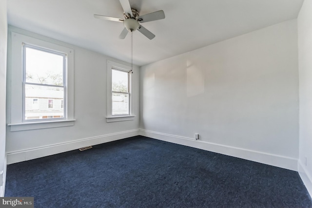 spare room featuring baseboards, dark carpet, and a ceiling fan