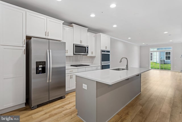 kitchen with light wood finished floors, a center island with sink, appliances with stainless steel finishes, crown molding, and a sink