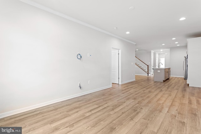 unfurnished living room with light wood finished floors, baseboards, stairway, crown molding, and a sink