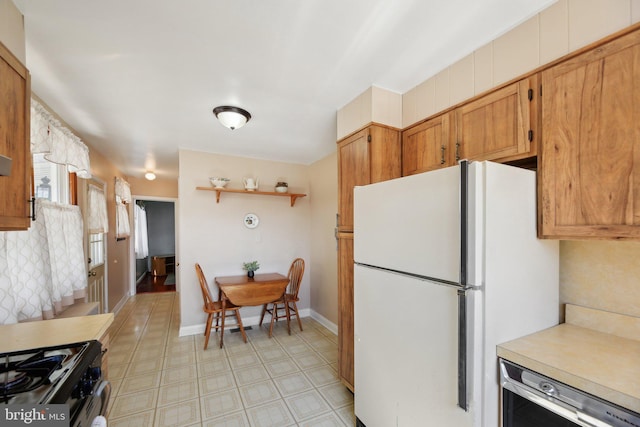 kitchen with beverage cooler, baseboards, freestanding refrigerator, light countertops, and brown cabinets