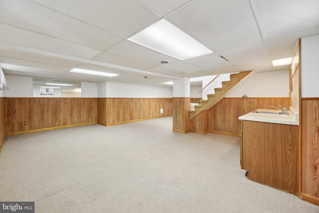 finished basement featuring a wainscoted wall, stairway, wooden walls, and a sink