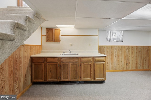 kitchen with wooden walls, a paneled ceiling, a wainscoted wall, and a sink