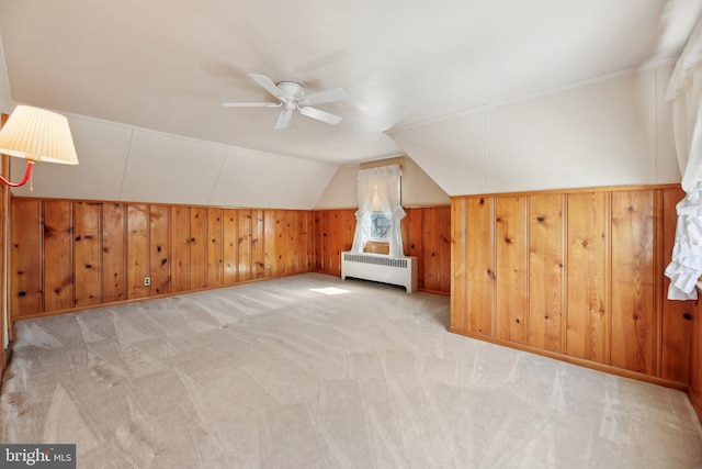 bonus room with wooden walls, a ceiling fan, radiator heating unit, vaulted ceiling, and light carpet