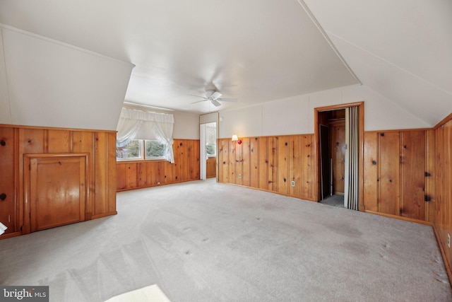 bonus room featuring a wainscoted wall, light carpet, wooden walls, ceiling fan, and vaulted ceiling