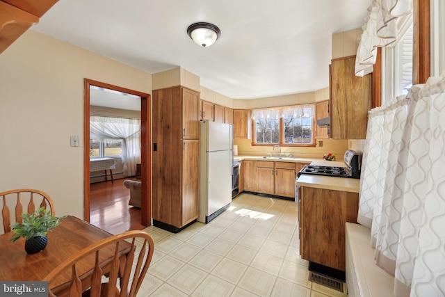 kitchen featuring a sink, freestanding refrigerator, light countertops, gas range, and baseboard heating