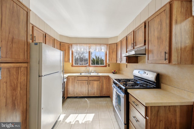 kitchen with stainless steel gas range, freestanding refrigerator, a sink, light countertops, and under cabinet range hood