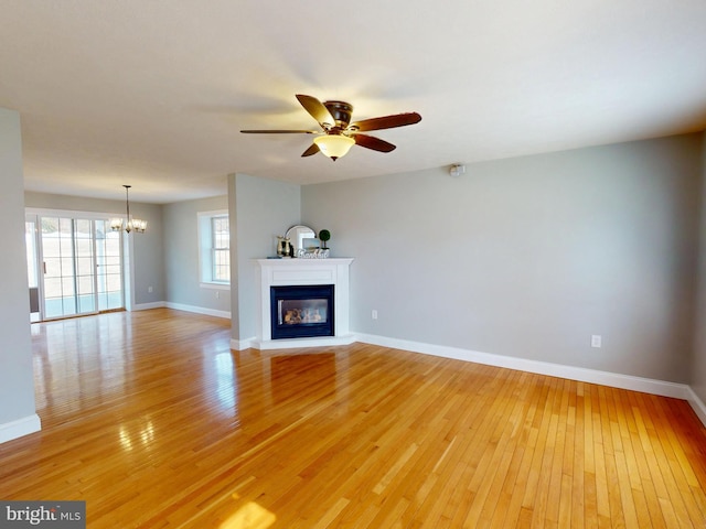 unfurnished living room with a glass covered fireplace, ceiling fan with notable chandelier, baseboards, and light wood-style floors