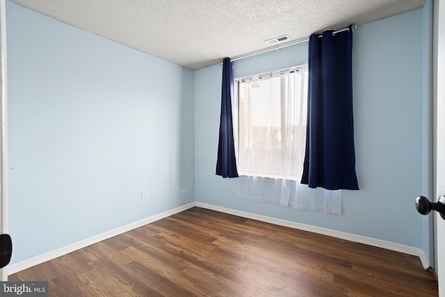 empty room with a textured ceiling, dark wood-type flooring, visible vents, and baseboards