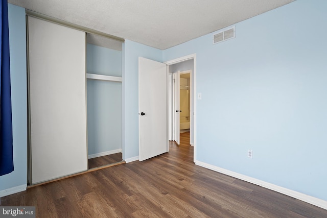 unfurnished bedroom with visible vents, a textured ceiling, baseboards, and wood finished floors