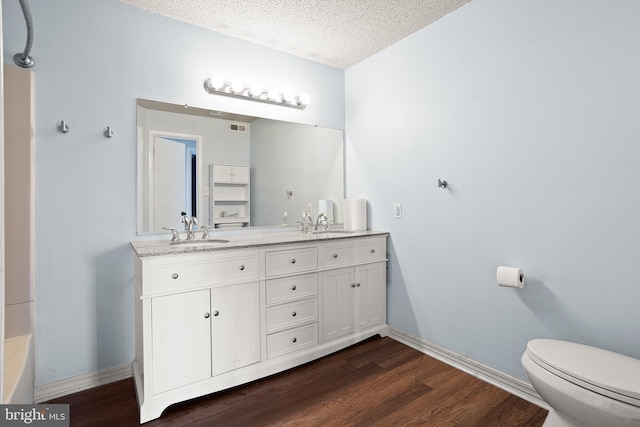 full bathroom with a textured ceiling, wood finished floors, a sink, and toilet