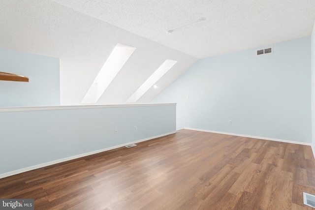 bonus room featuring vaulted ceiling with skylight, a textured ceiling, visible vents, and wood finished floors