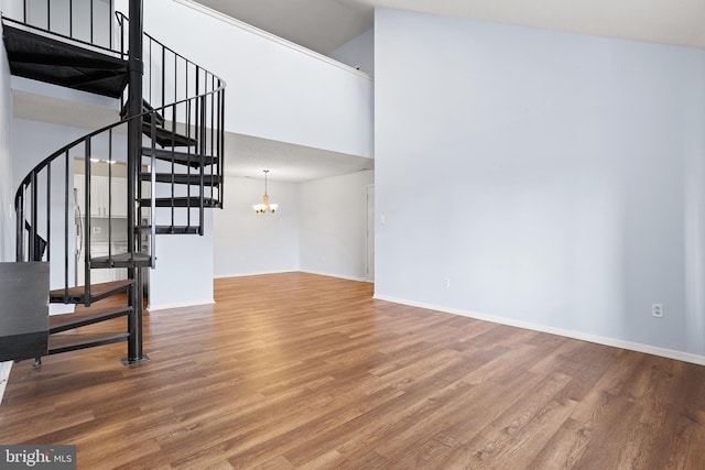 unfurnished living room featuring baseboards, stairway, wood finished floors, a high ceiling, and a chandelier