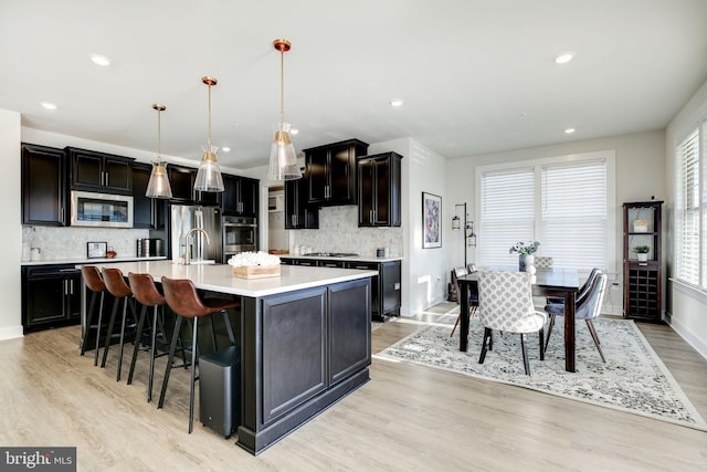 kitchen with a spacious island, appliances with stainless steel finishes, light countertops, light wood-type flooring, and a sink