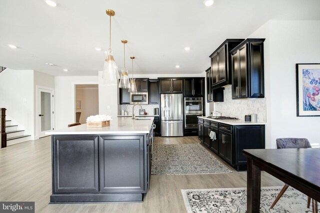 kitchen with light countertops, appliances with stainless steel finishes, a sink, an island with sink, and light wood-type flooring