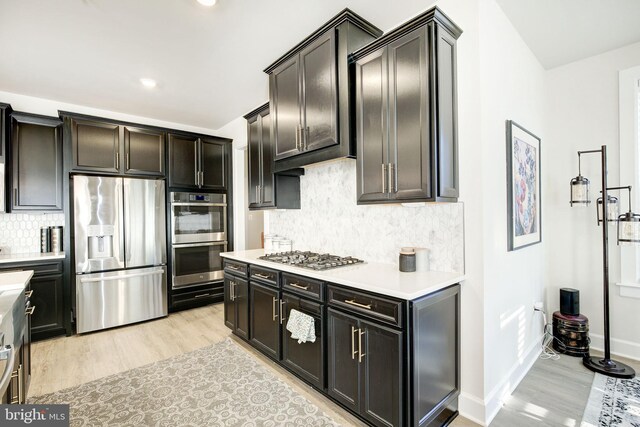 kitchen with baseboards, appliances with stainless steel finishes, light countertops, light wood-type flooring, and backsplash