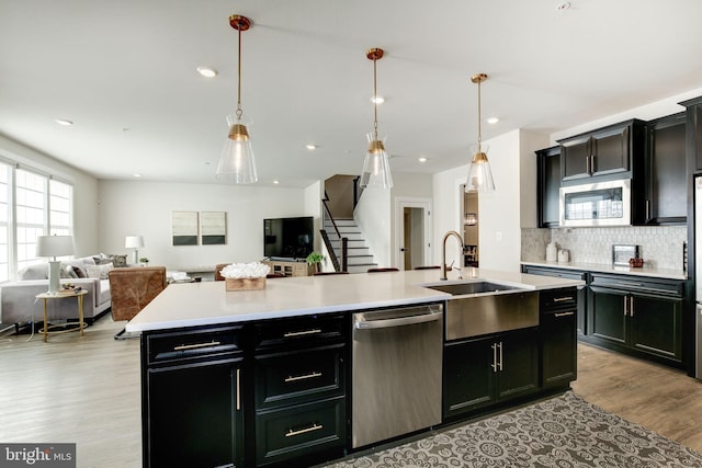 kitchen featuring a center island with sink, stainless steel appliances, light countertops, open floor plan, and dark cabinetry