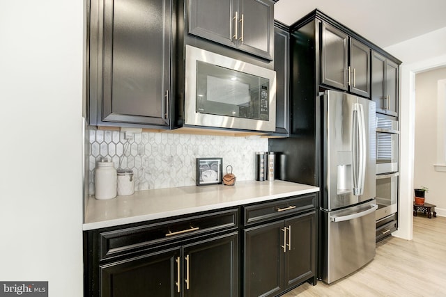 kitchen featuring light wood-style flooring, dark cabinets, stainless steel appliances, light countertops, and tasteful backsplash