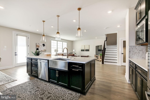 kitchen featuring dark cabinets, wood finished floors, light countertops, appliances with stainless steel finishes, and tasteful backsplash