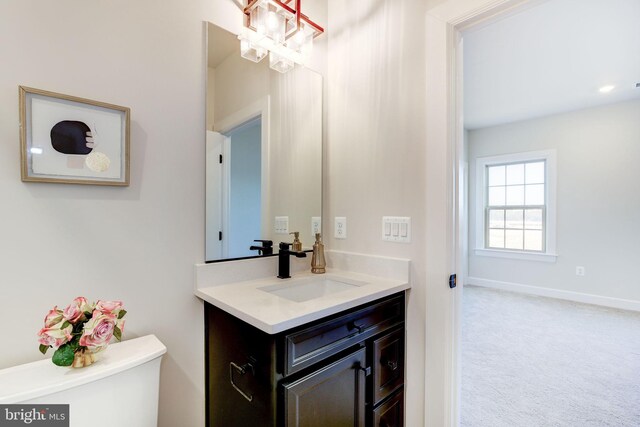 half bath with baseboards, vanity, toilet, and an inviting chandelier