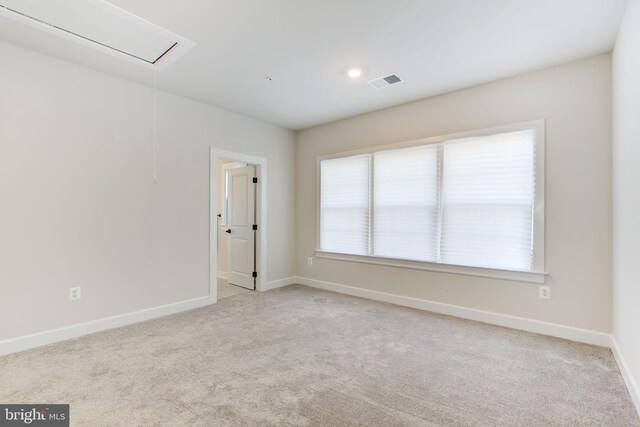 carpeted spare room featuring visible vents, attic access, and baseboards