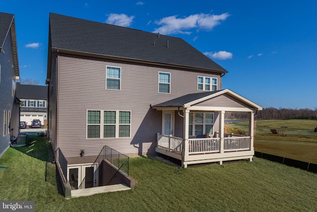 back of property featuring a shingled roof, a deck, and a lawn