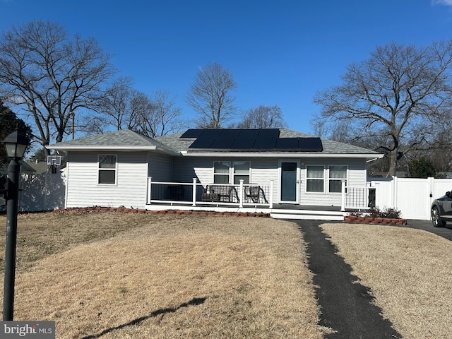 ranch-style home featuring driveway, fence, roof mounted solar panels, a porch, and a front yard