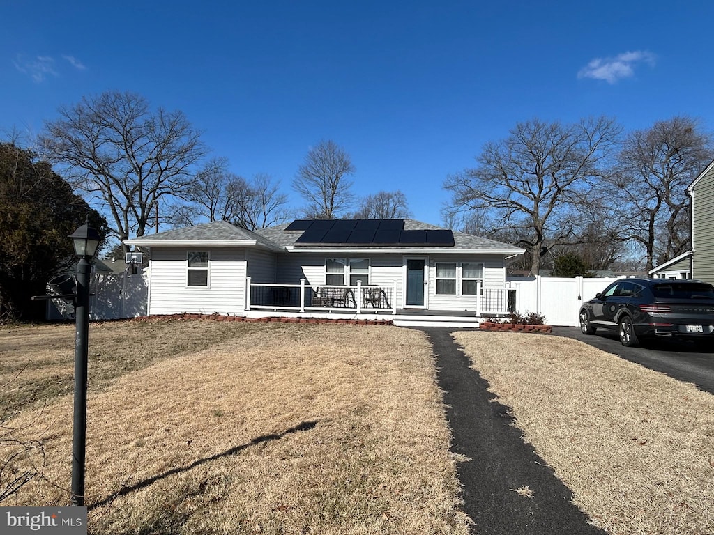 ranch-style house with covered porch, fence, driveway, roof mounted solar panels, and a front yard