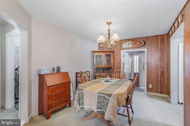 dining room featuring wooden walls, baseboards, arched walkways, light colored carpet, and a notable chandelier