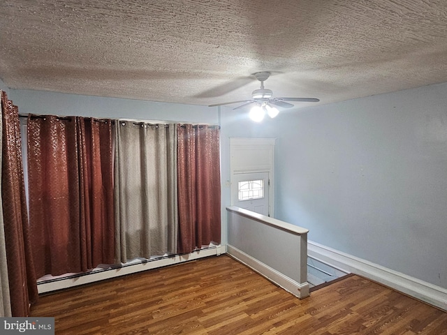 empty room featuring baseboards, ceiling fan, wood finished floors, baseboard heating, and a textured ceiling