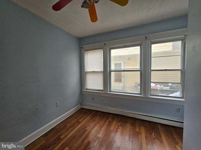 unfurnished room featuring baseboard heating, dark wood finished floors, and a healthy amount of sunlight