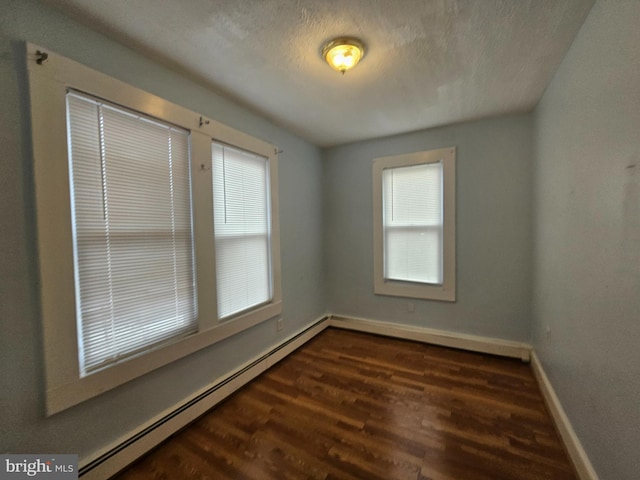 unfurnished room with a baseboard heating unit, a textured ceiling, wood finished floors, and a wealth of natural light