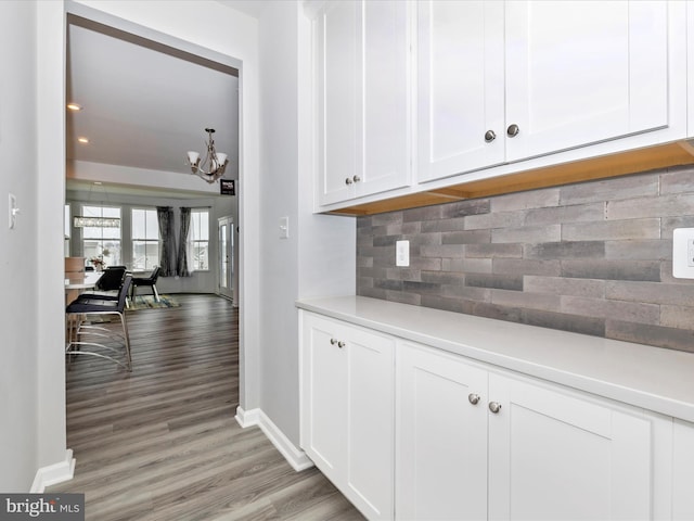 kitchen with decorative backsplash, light countertops, light wood-style floors, white cabinetry, and a notable chandelier