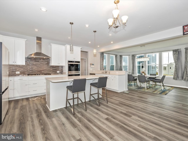 kitchen featuring light countertops, appliances with stainless steel finishes, wall chimney exhaust hood, tasteful backsplash, and a center island