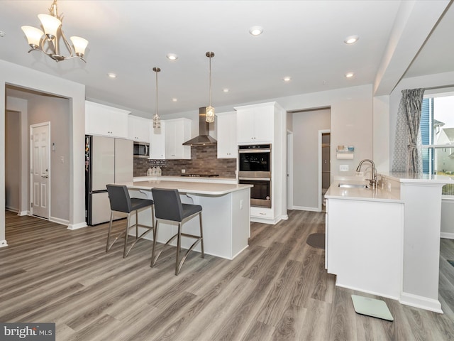 kitchen featuring appliances with stainless steel finishes, light countertops, wall chimney exhaust hood, and a sink