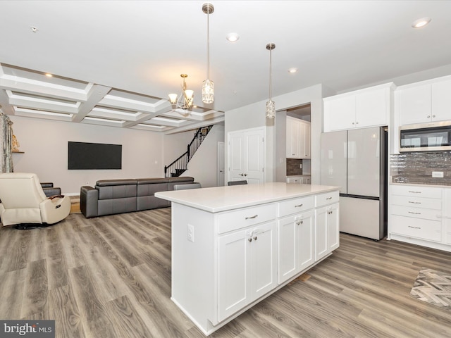 kitchen with coffered ceiling, an inviting chandelier, light wood-style flooring, freestanding refrigerator, and stainless steel microwave