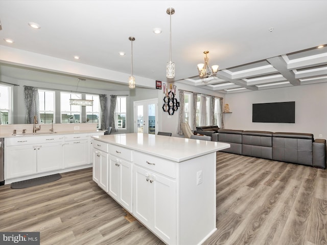 kitchen with light wood finished floors, a kitchen island, light countertops, an inviting chandelier, and coffered ceiling