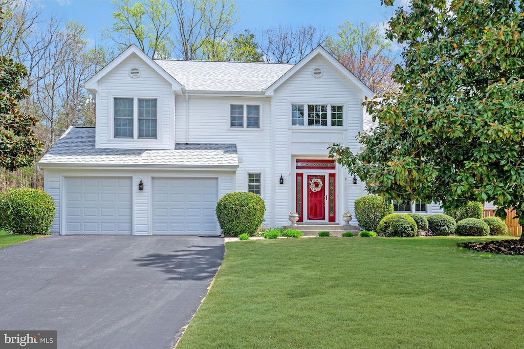 traditional home with a front lawn, an attached garage, aphalt driveway, and a shingled roof