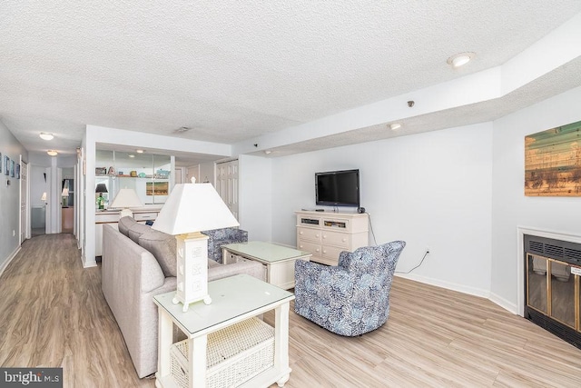 living room with light wood-style floors, a glass covered fireplace, a textured ceiling, and baseboards