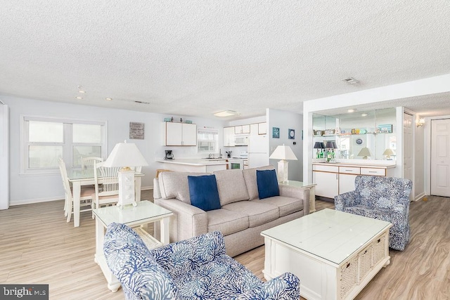 living area with light wood finished floors, visible vents, baseboards, and a textured ceiling