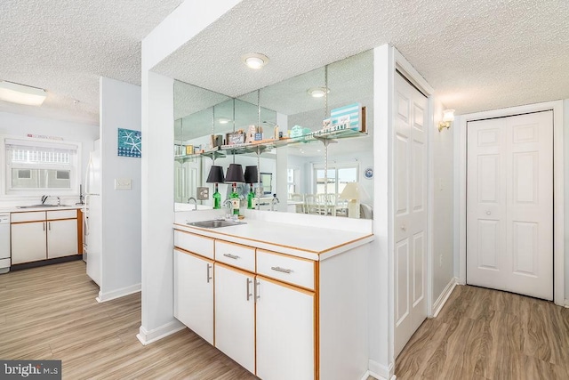 interior space with light wood-style flooring, white dishwasher, a sink, a textured ceiling, and baseboards