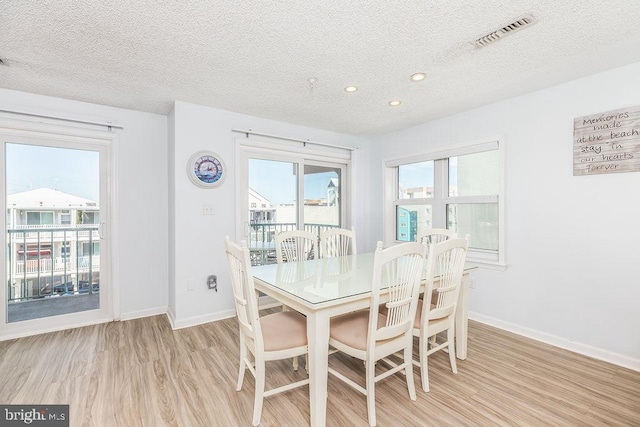 dining room with light wood-style flooring, a textured ceiling, visible vents, and baseboards