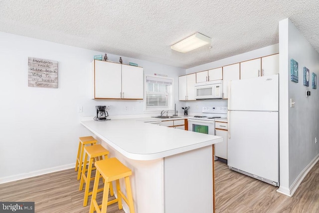 kitchen featuring white appliances, a breakfast bar, a peninsula, light countertops, and light wood-type flooring