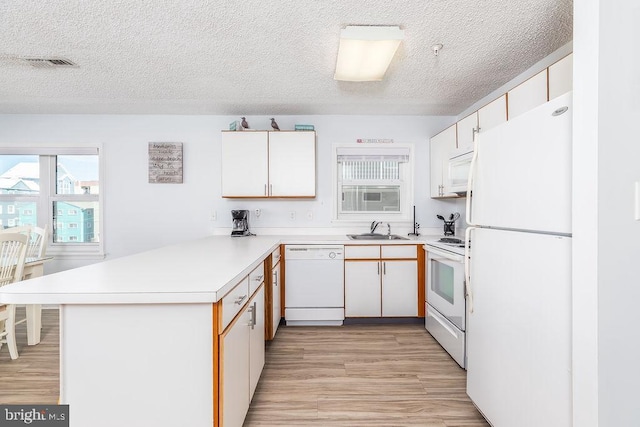 kitchen with a peninsula, white appliances, a sink, visible vents, and light countertops