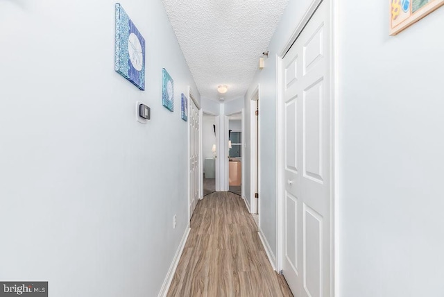 corridor featuring baseboards, a textured ceiling, and light wood finished floors