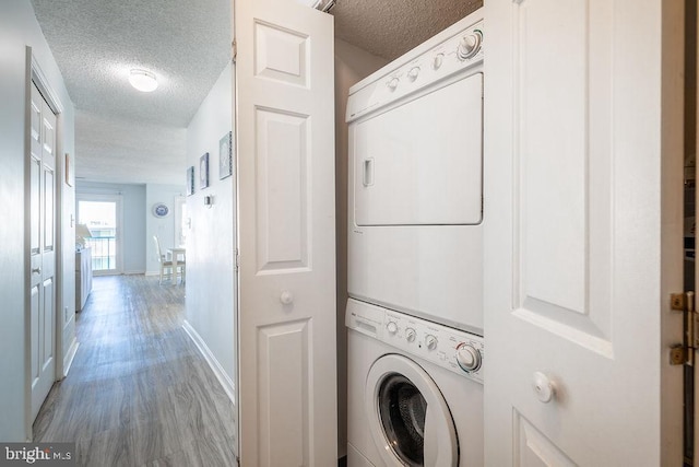 laundry room featuring a textured ceiling, light wood-style flooring, laundry area, baseboards, and stacked washer and clothes dryer